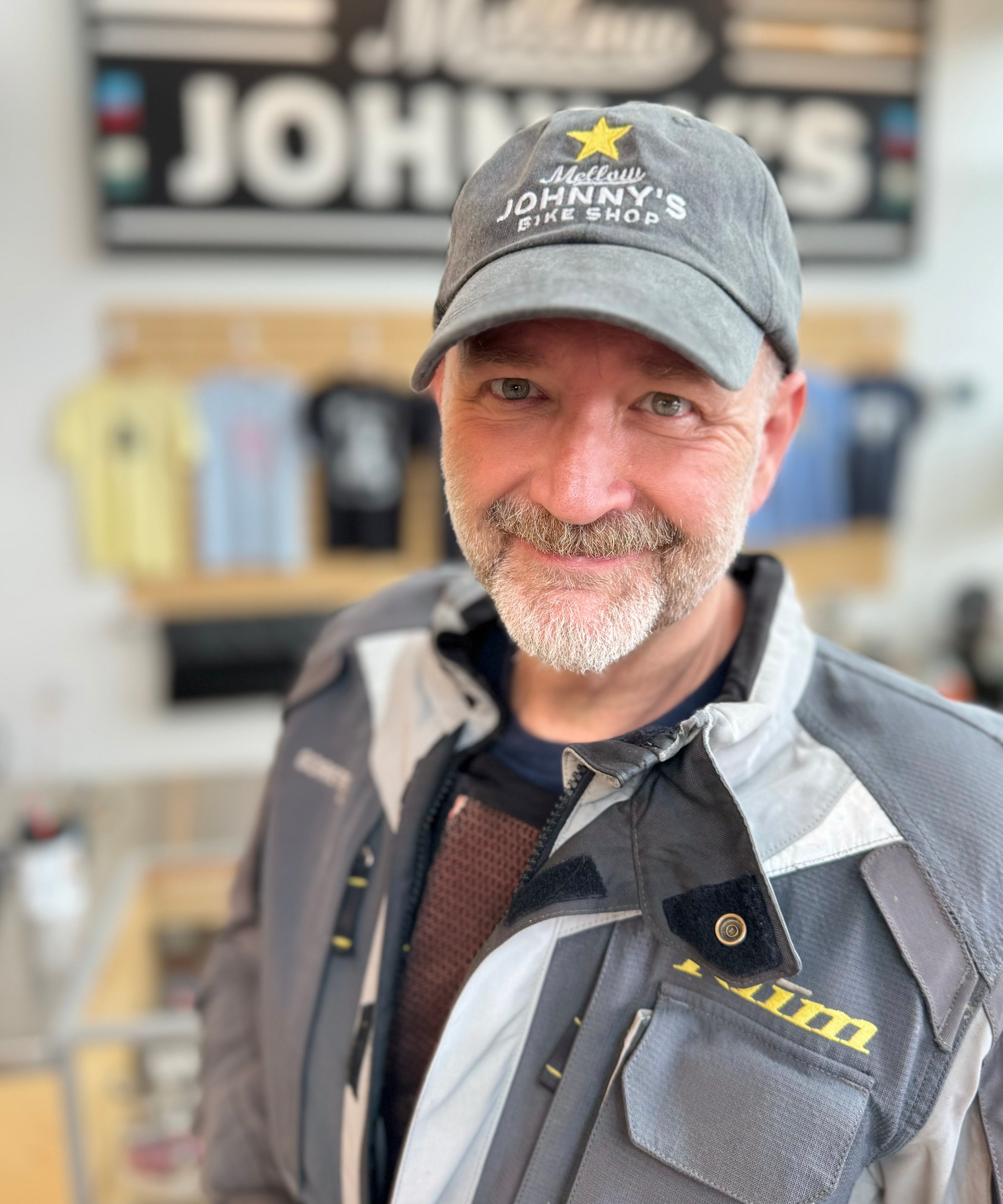 A person wearing a gray baseball cap with a Mellow Johnny's logo on it, standing in front of a store counter.
